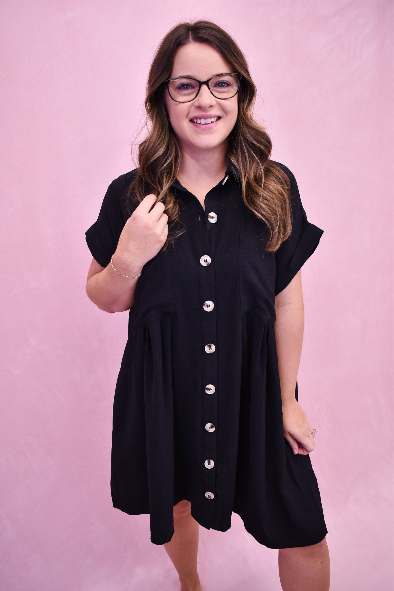 Woman wearing a black button-up dress against a pink background