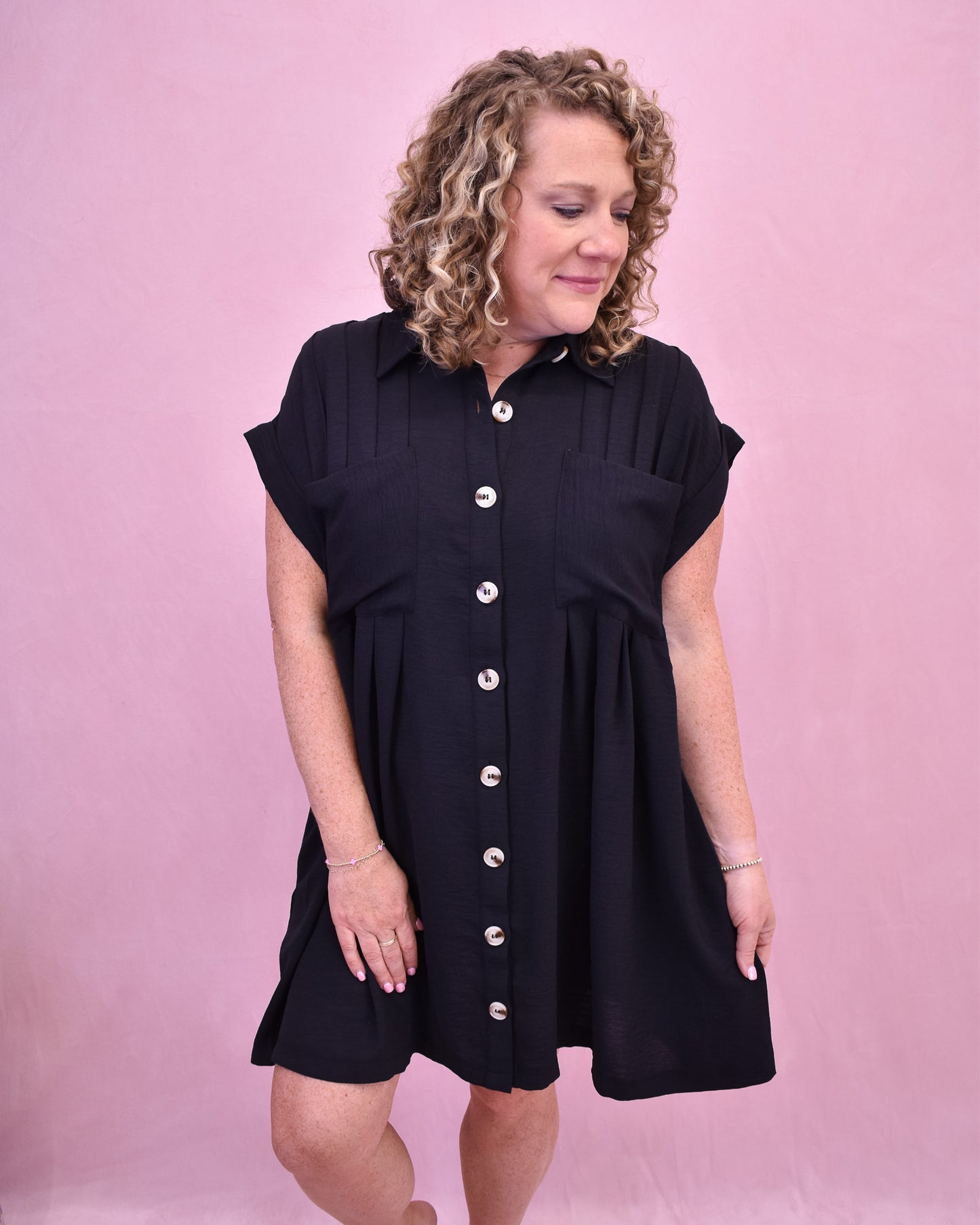 Woman wearing a black dress with buttons on a pink background