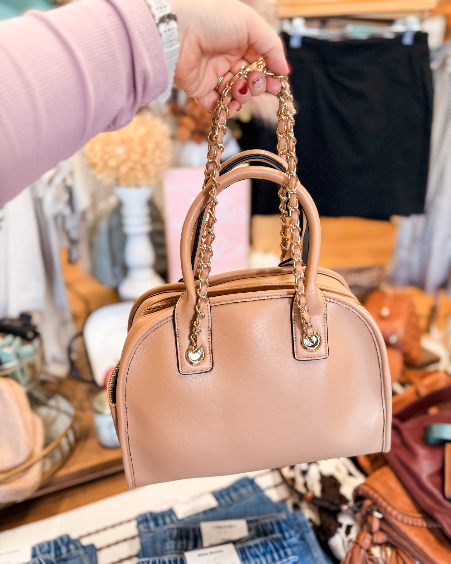 Beige handbag with chain handle held by a person in a clothing store.