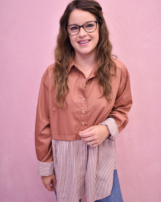 Woman wearing a brown shirt over a striped shirt with a pink background