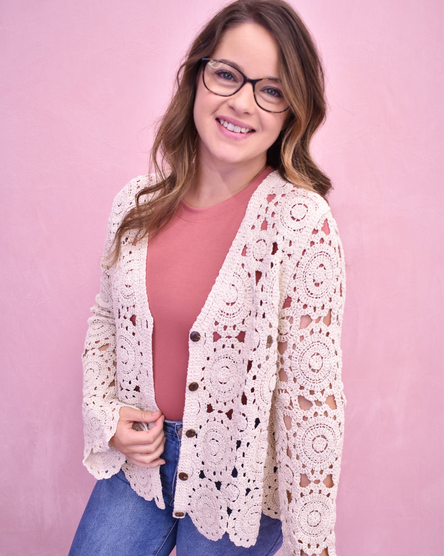 Woman wearing a white crochet cardigan over a pink shirt on a pink background