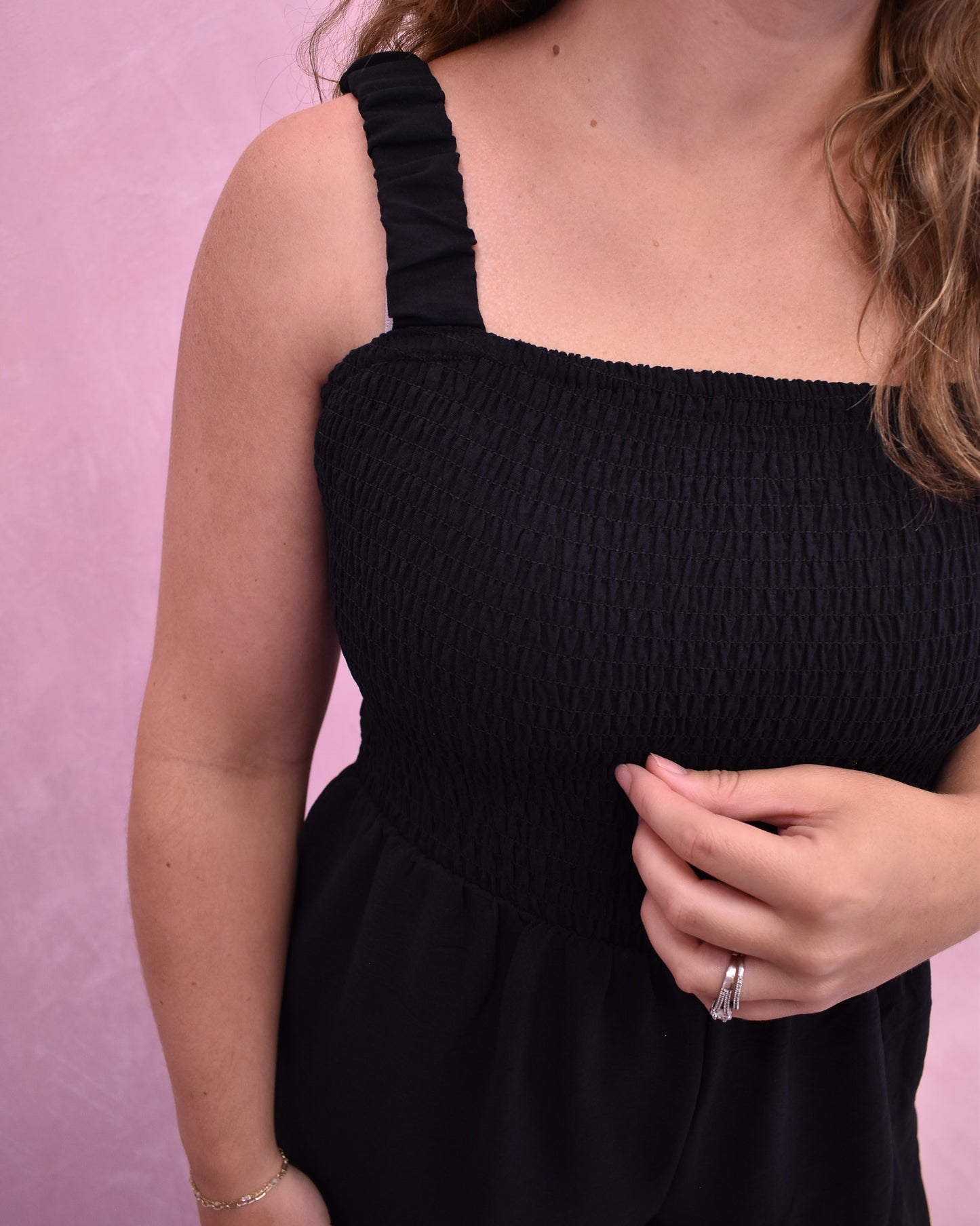 Person wearing a black sleeveless dress against a pink background