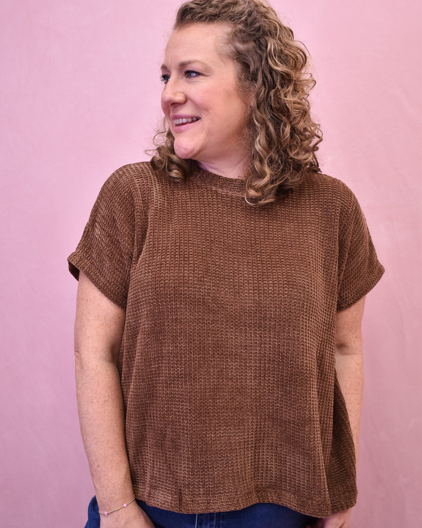 Woman wearing a brown textured sweater against a pink background