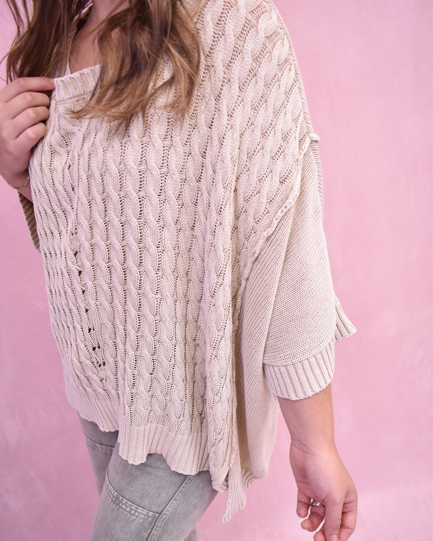 Person wearing a beige cable knit sweater against a pink background