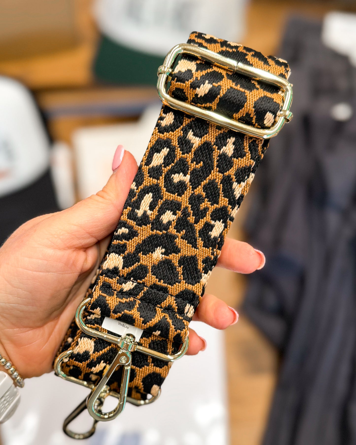 Leopard print strap with gold buckle held by a hand against a blurred indoor background