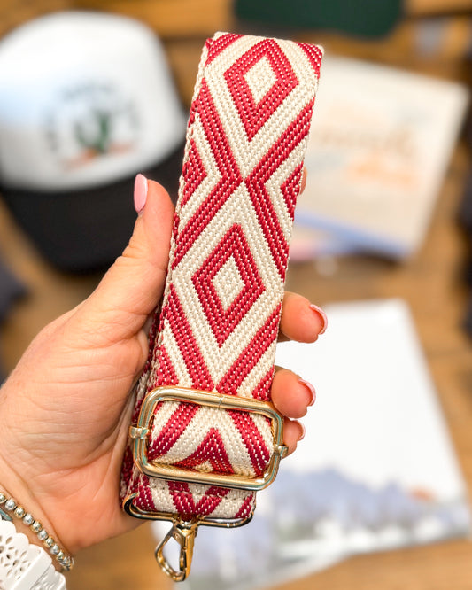 Hand holding a red and white beaded bag strap with a blurred background