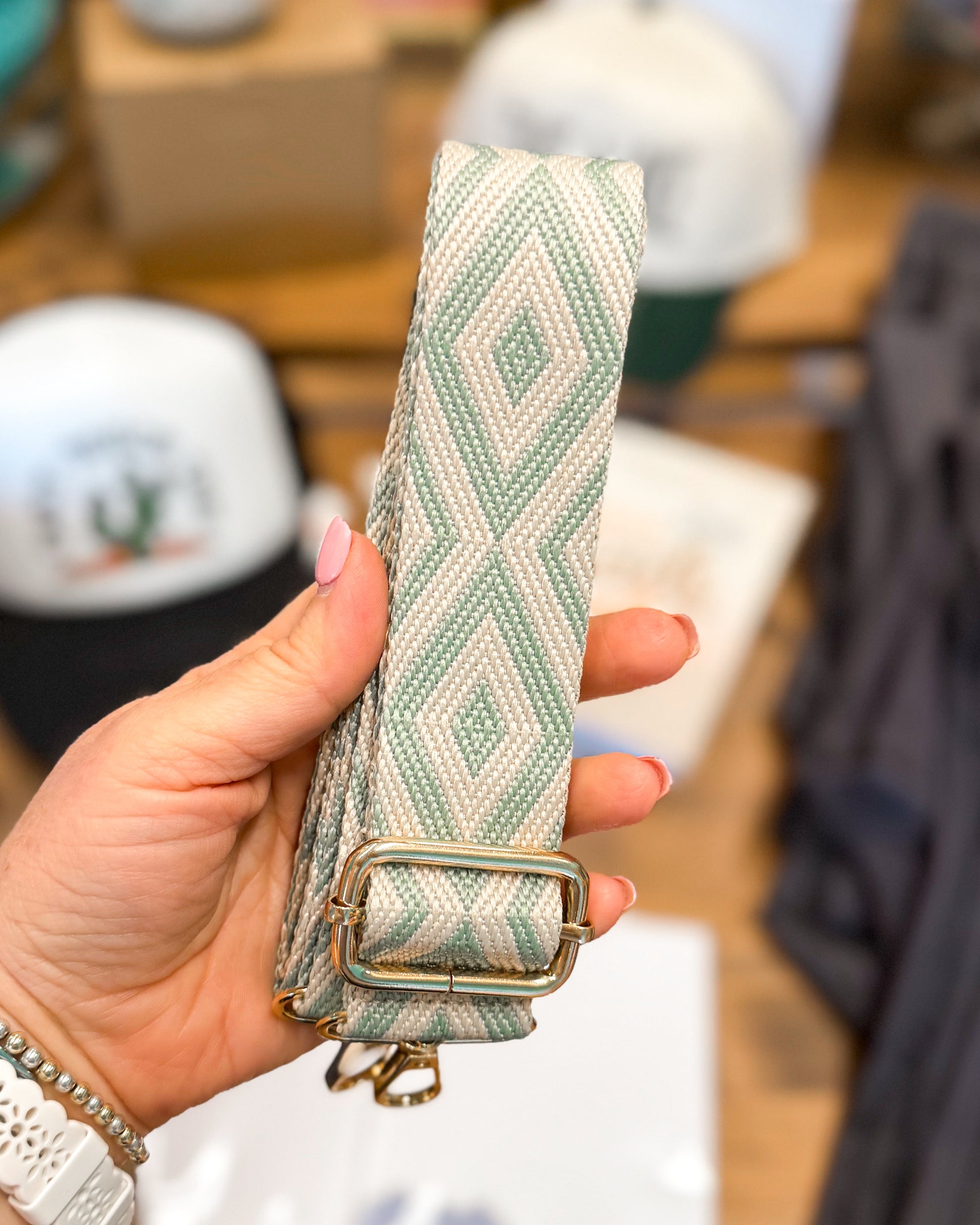 Hand holding a green woven belt with a gold buckle against a blurred indoor background