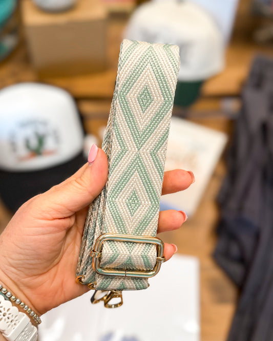 Hand holding a green woven belt with a gold buckle against a blurred indoor background