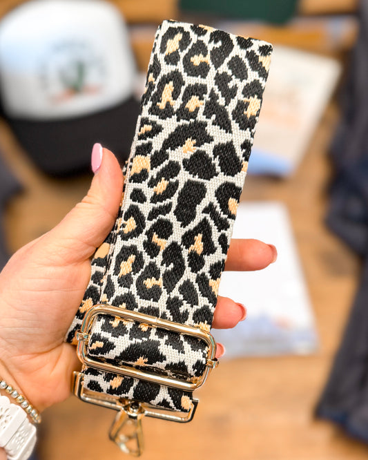 Leopard print belt with a gold buckle held by a hand against a blurred background