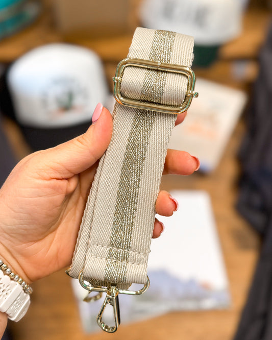 Hand holding a beige belt with a gold buckle against a blurred indoor background