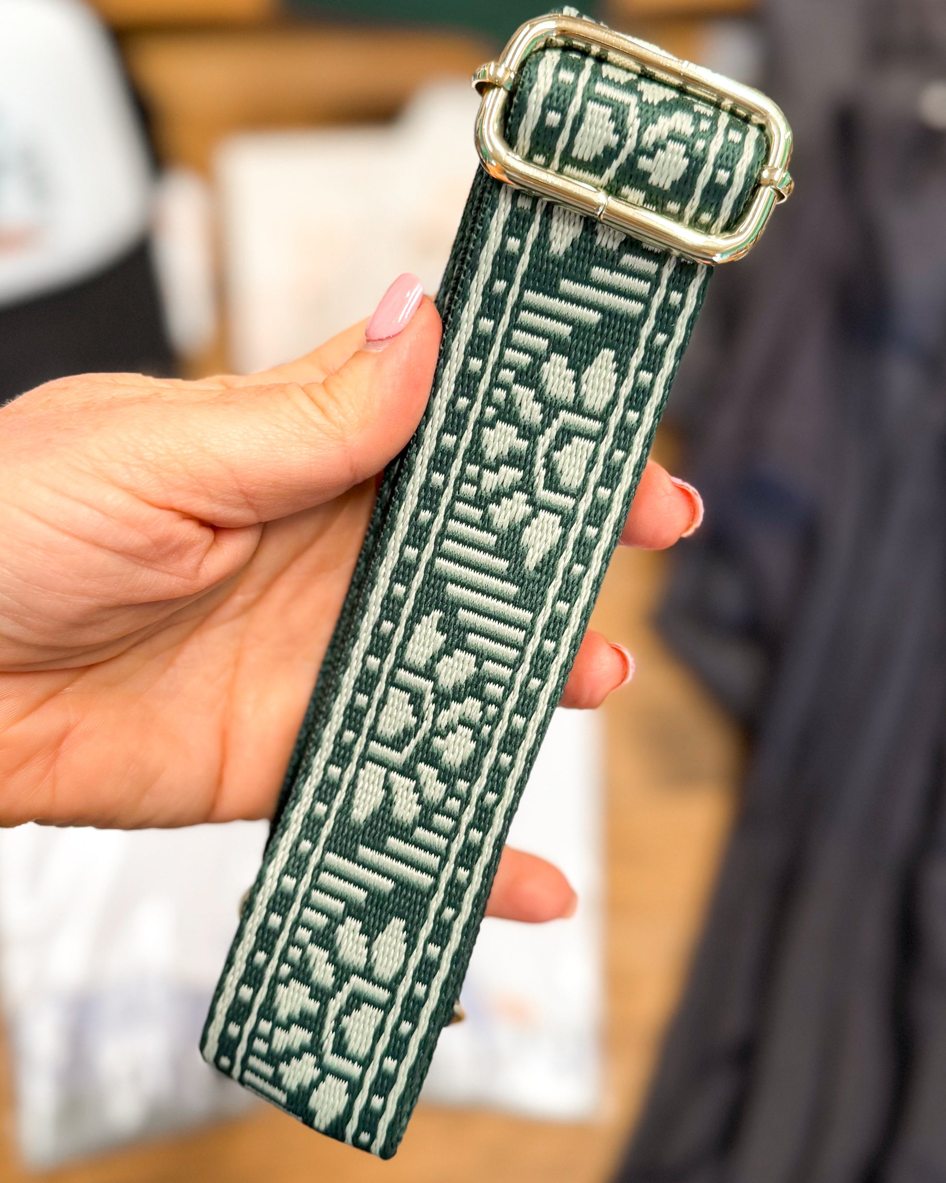 Hand holding a green textured strap with a metal buckle against a blurred background