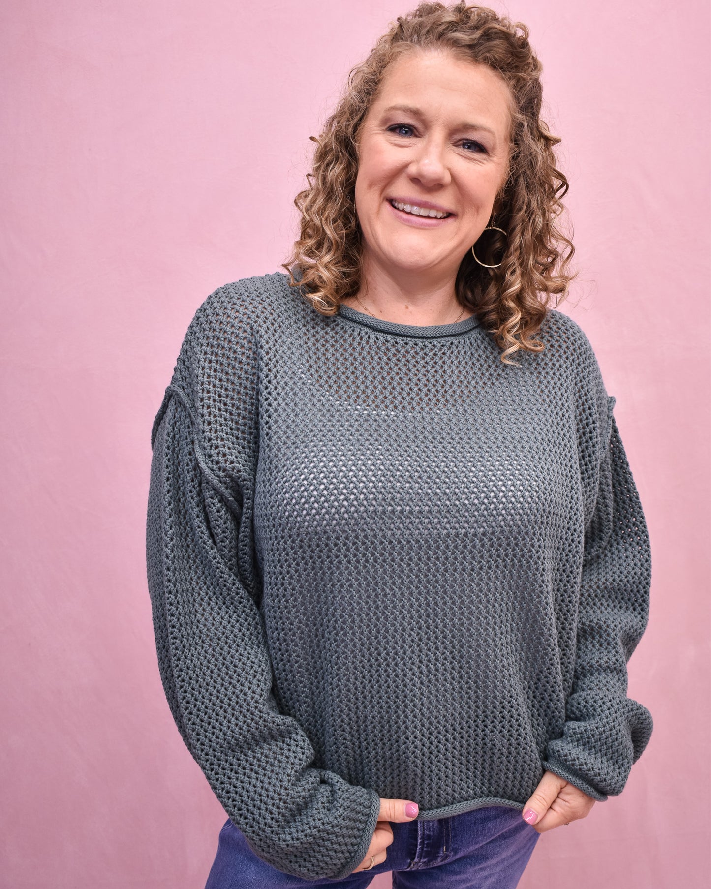 Woman wearing a textured gray sweater against a pink background