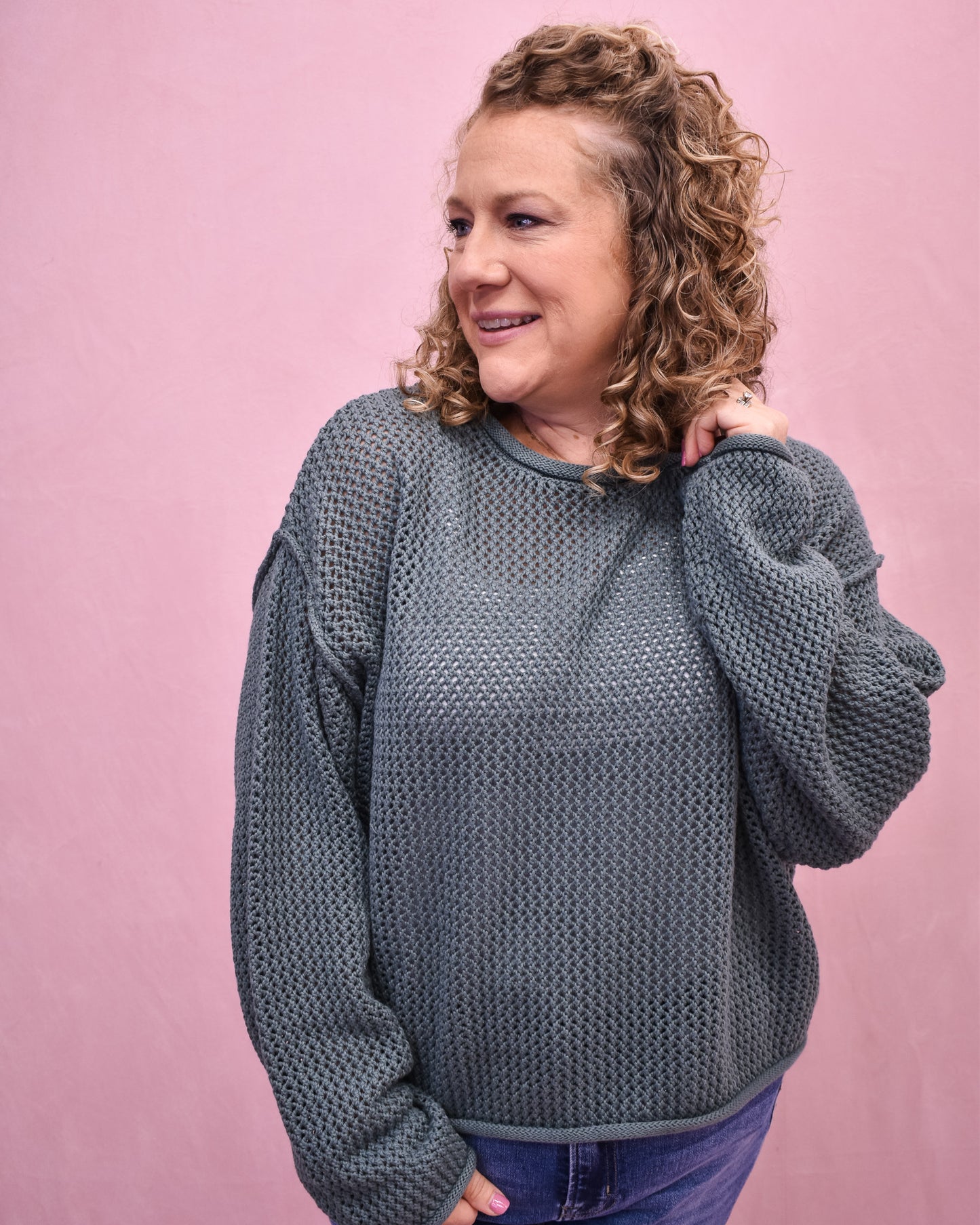 Woman wearing a textured gray sweater against a pink background