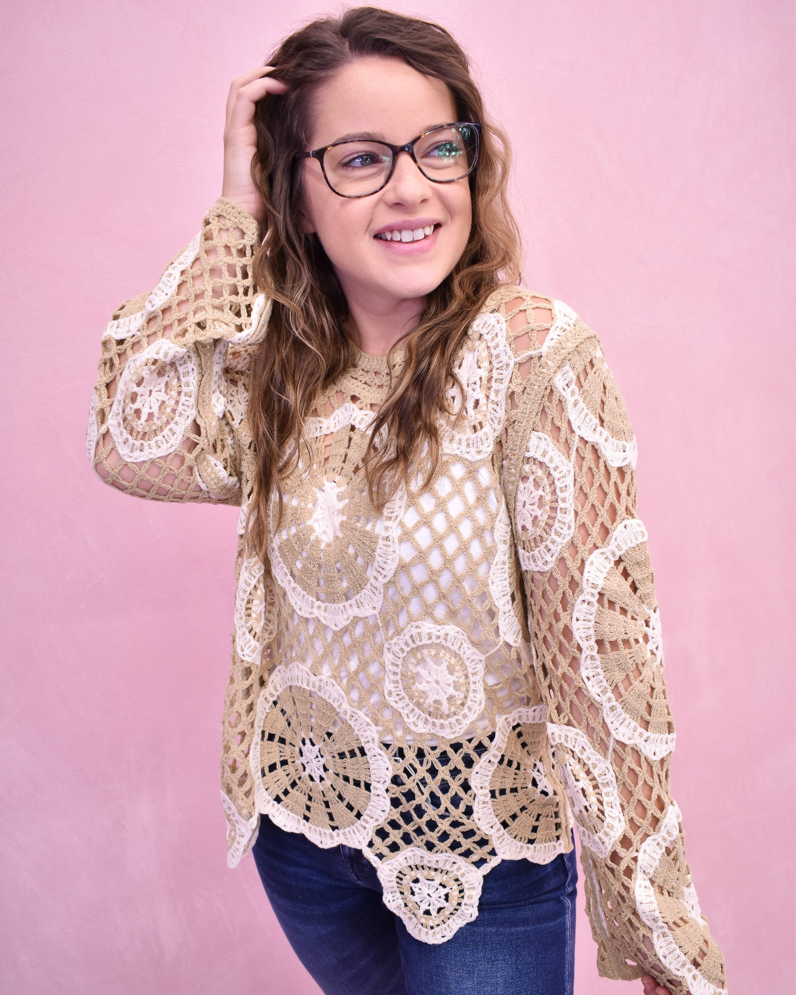 Woman wearing a beige crochet top against a pink background