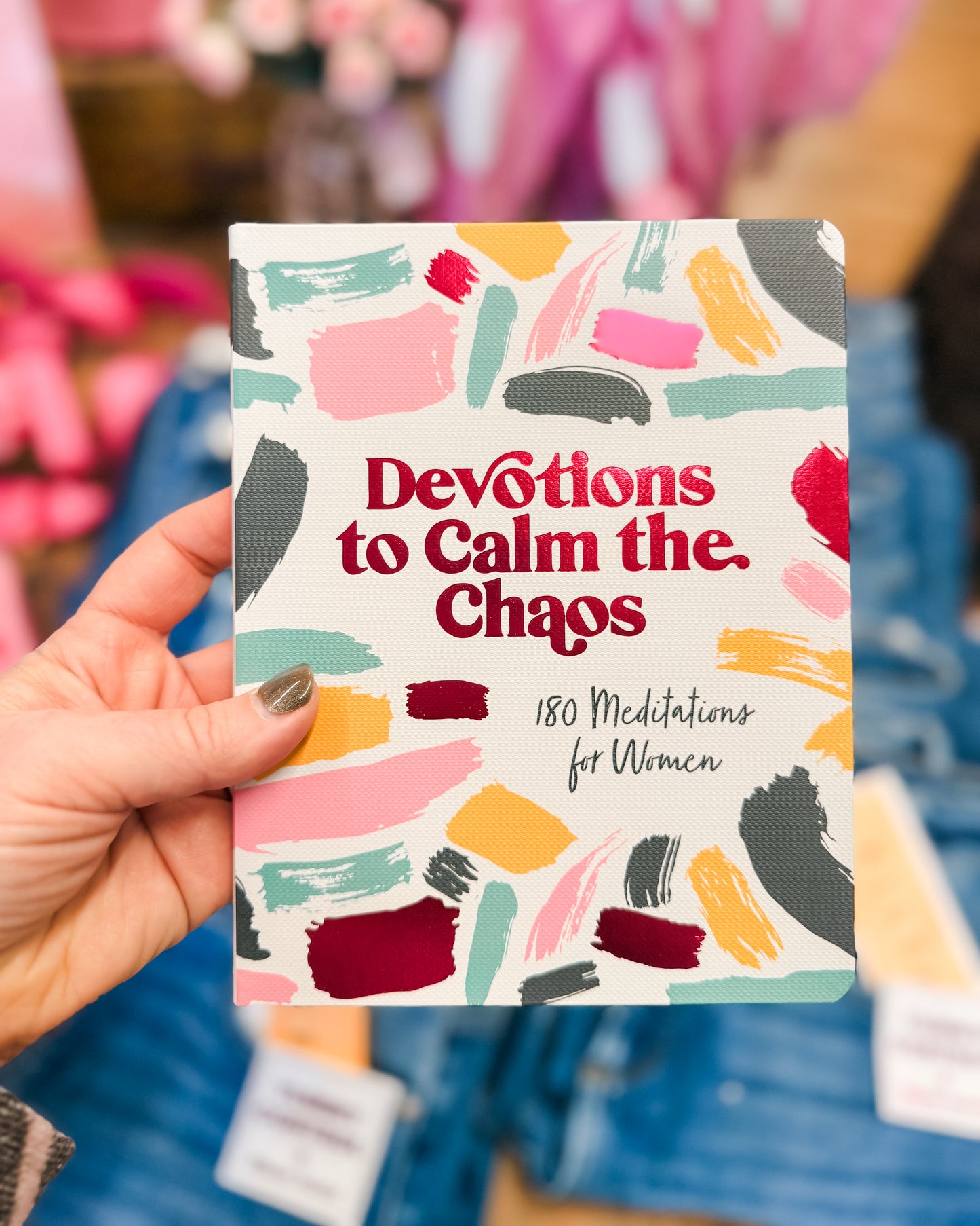 Book titled 'Devotions to Calm the Chaos' held by a hand with a colorful cover.