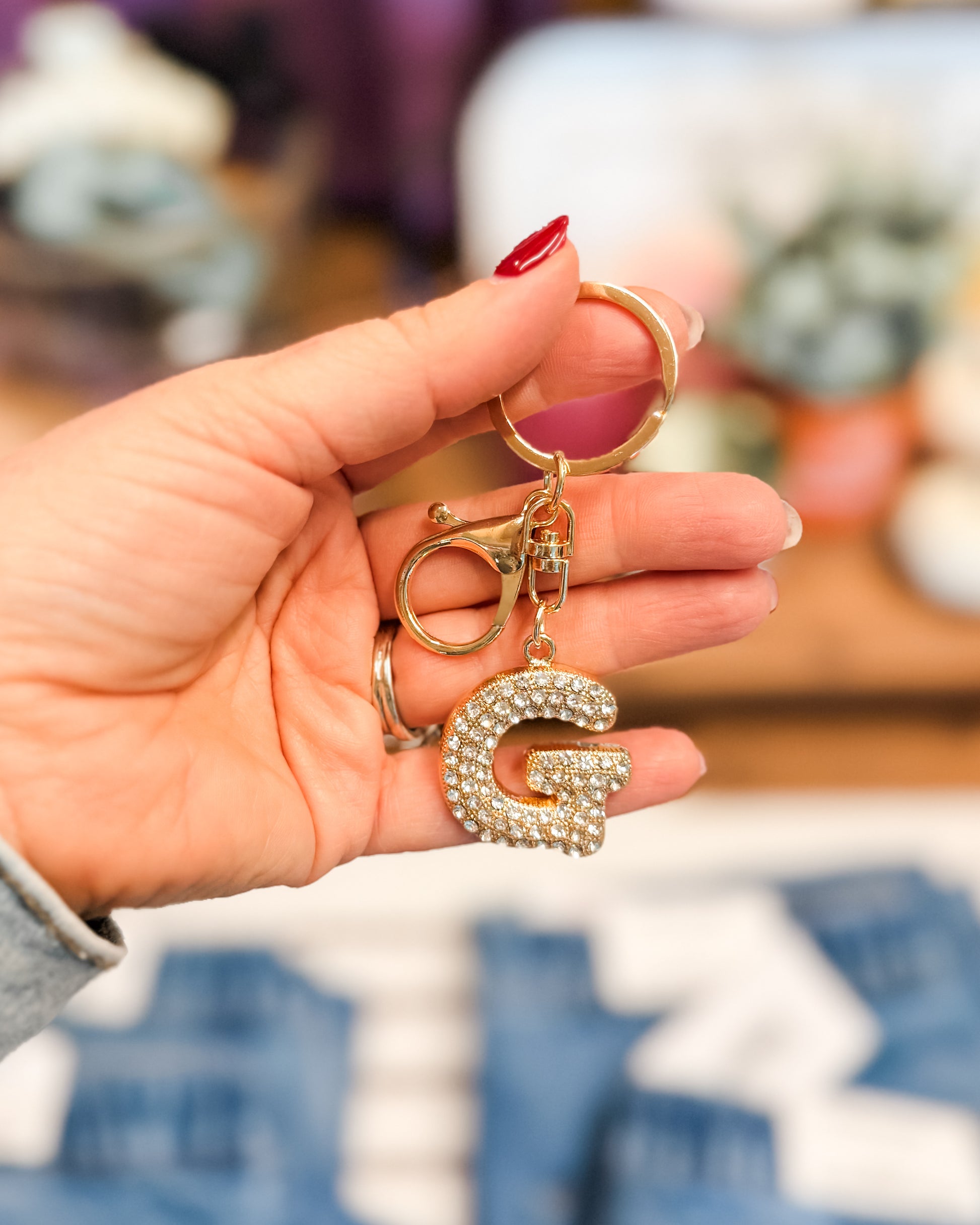Hand holding a keychain with a letter 'G' charm against a blurred background