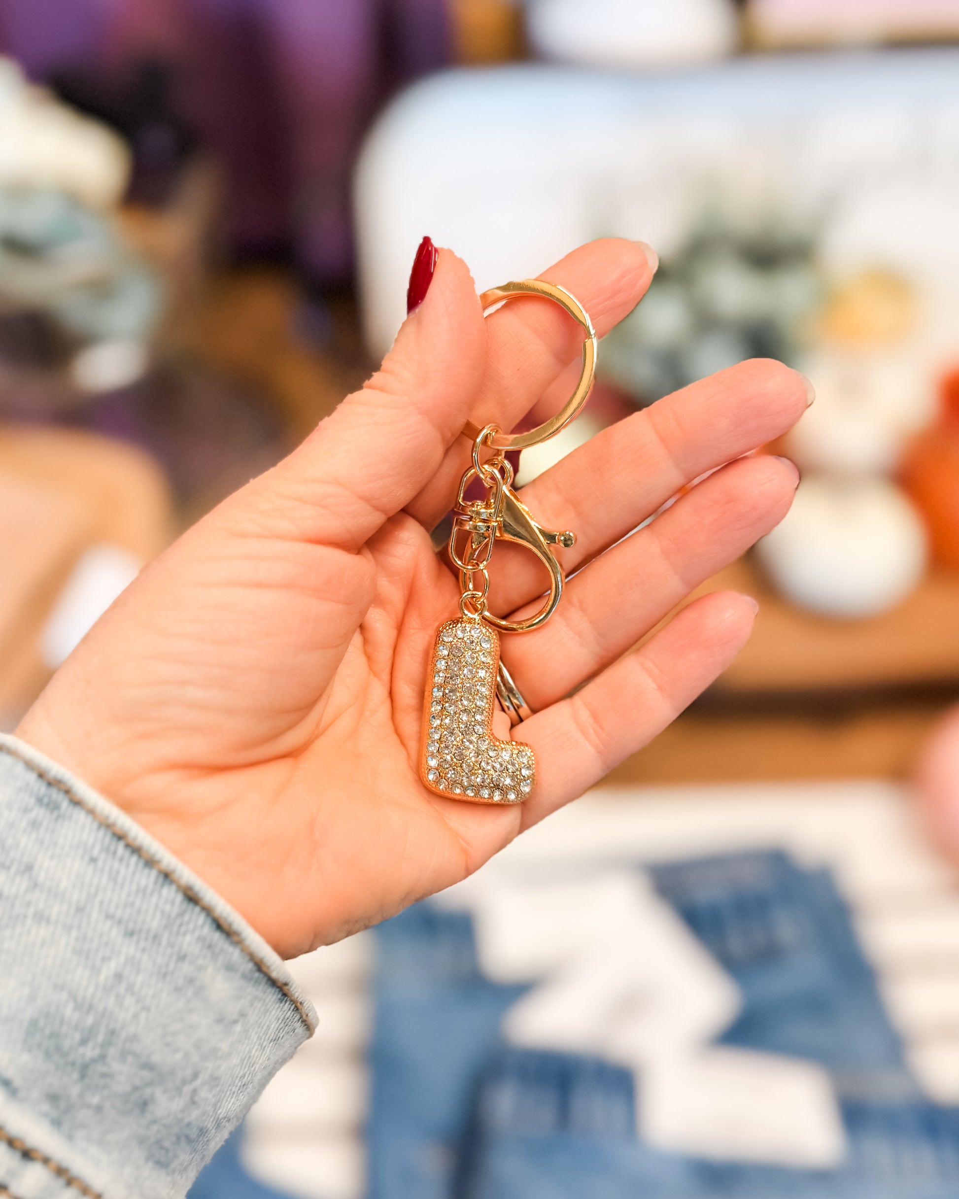Hand holding a keychain with a decorative letter 'L' charm against a blurred indoor background