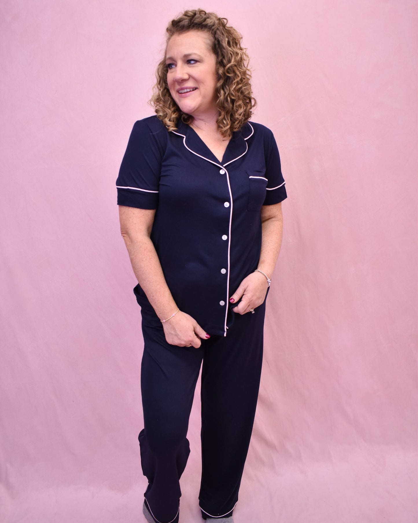 Woman wearing a navy pajama set with white buttons against a pink background
