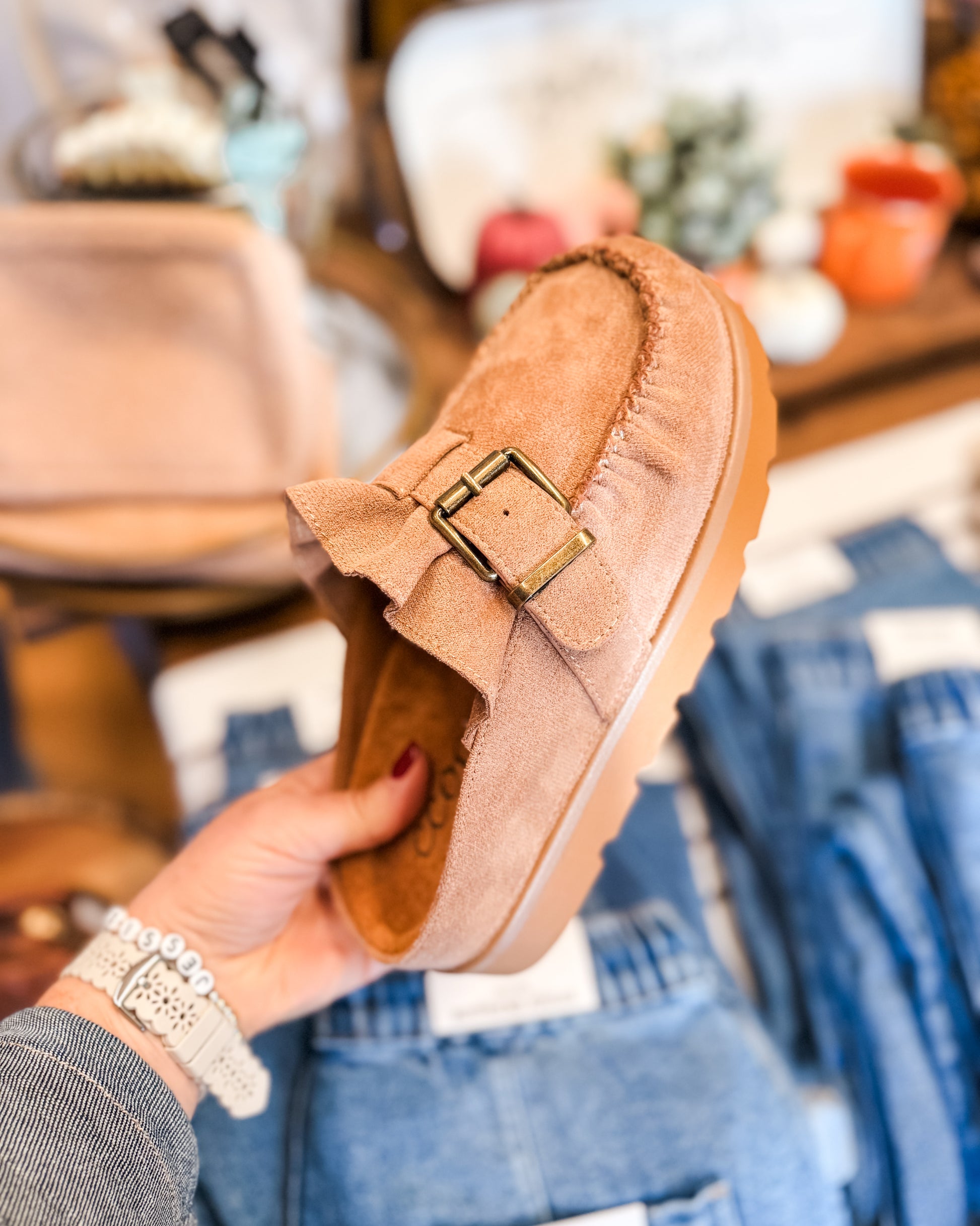 Tan suede loafer with a buckle held by a hand in a store setting