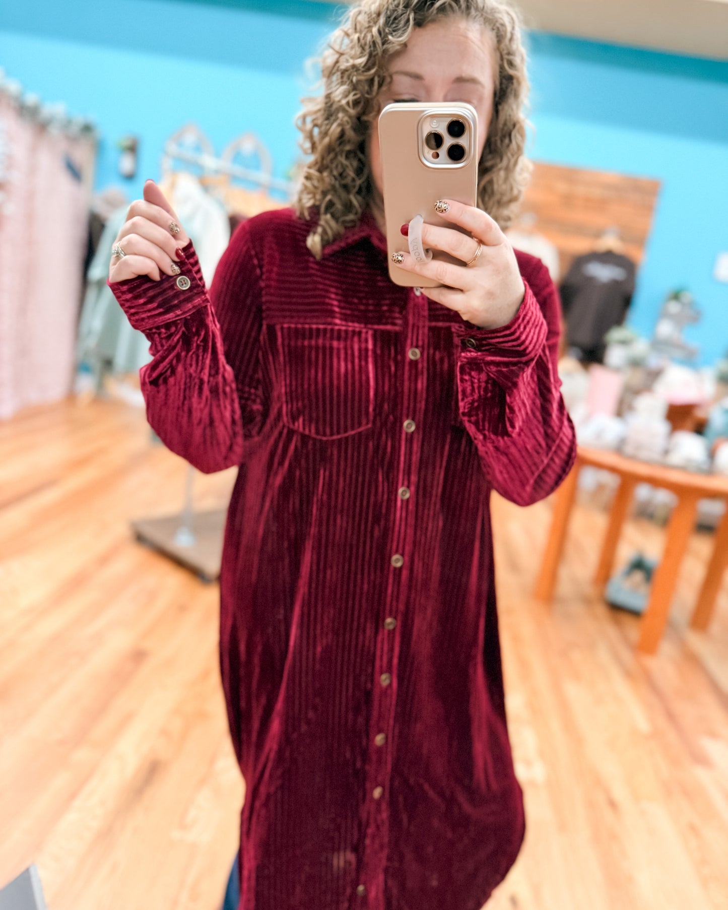 Person wearing a red corduroy dress taking a mirror selfie in a store.