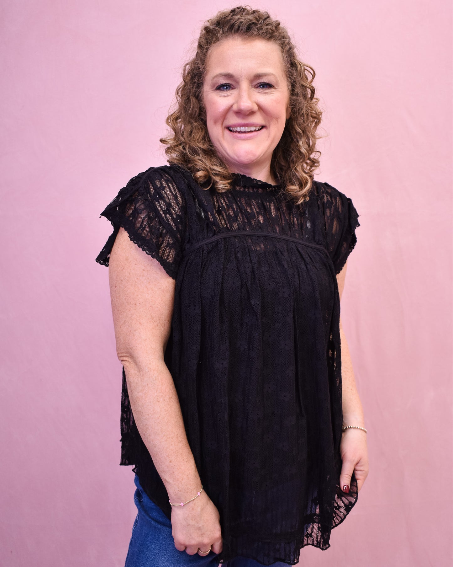 Woman wearing a black lace top against a pink background