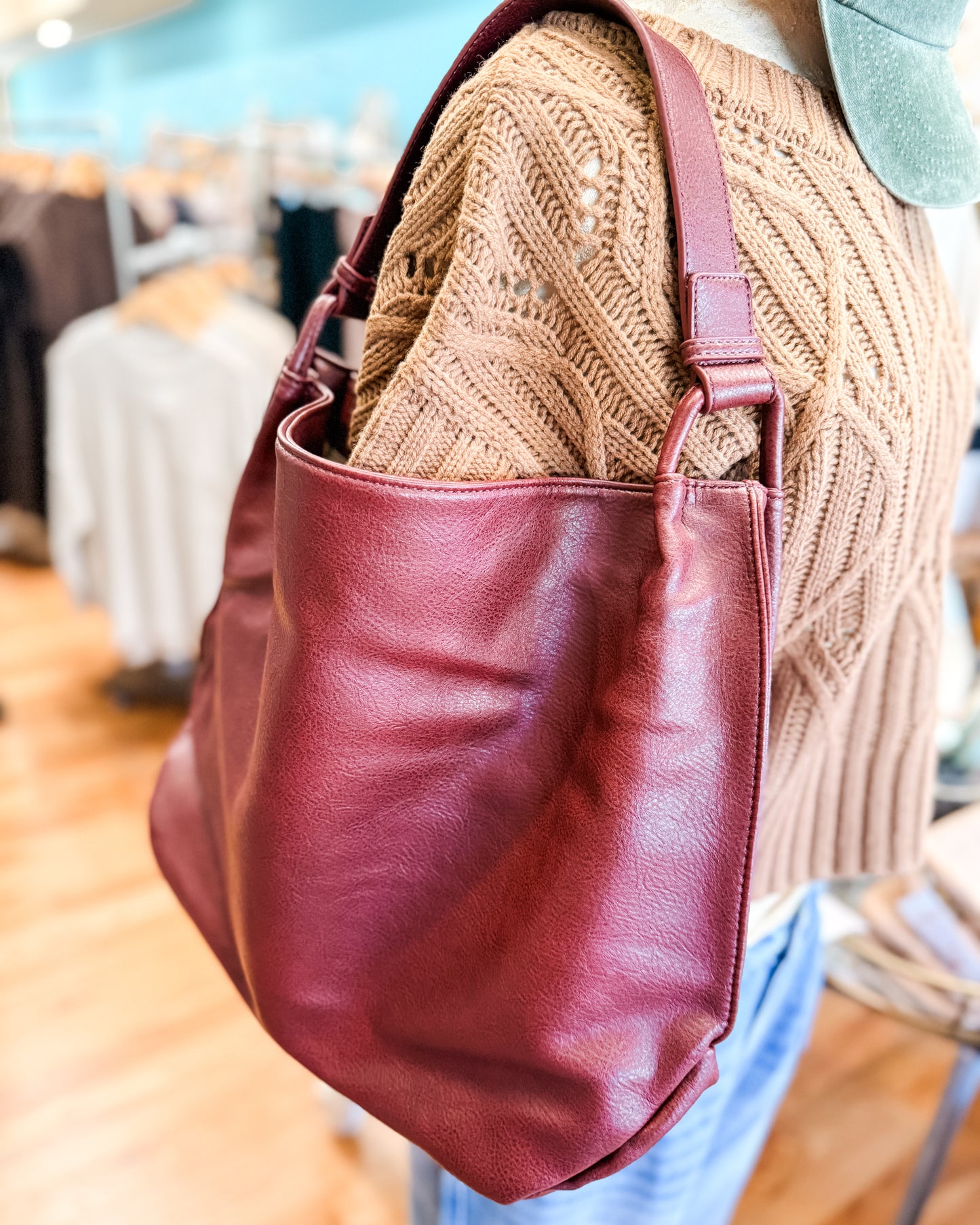 Maroon leather handbag held by a person wearing a beige knitted sweater.