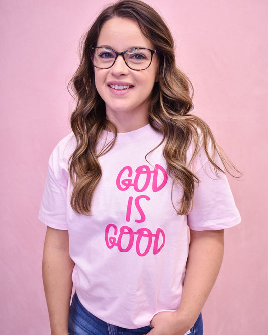 Person wearing a pink t-shirt with 'GOD IS GOOD' text on a pink background