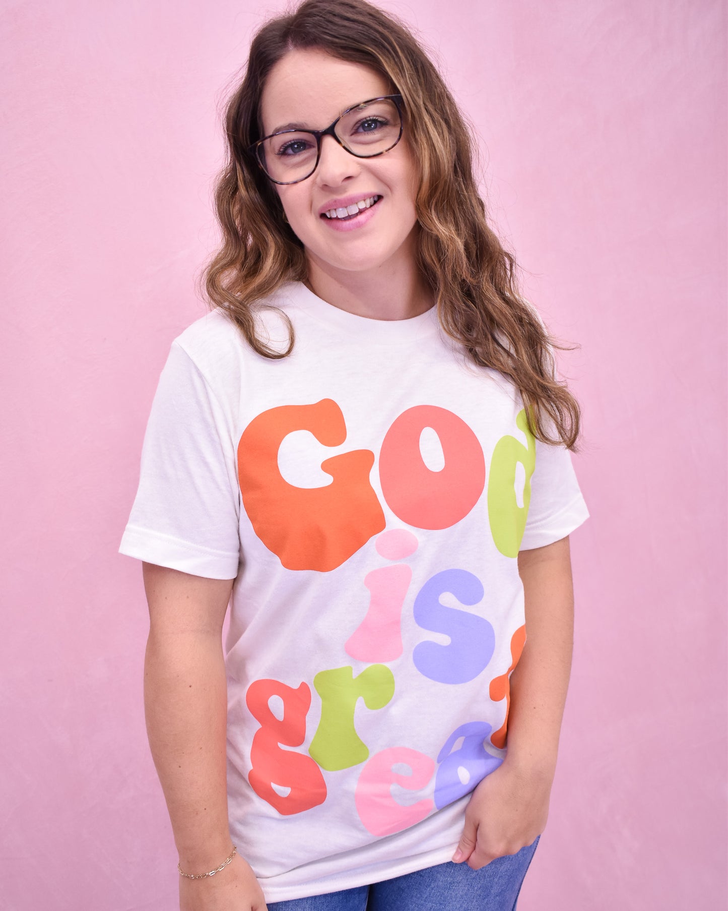 Person wearing a white t-shirt with colorful letters on a pink background