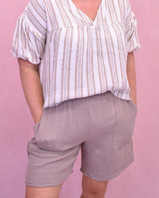 Person wearing a striped shirt and gray shorts against a pink background