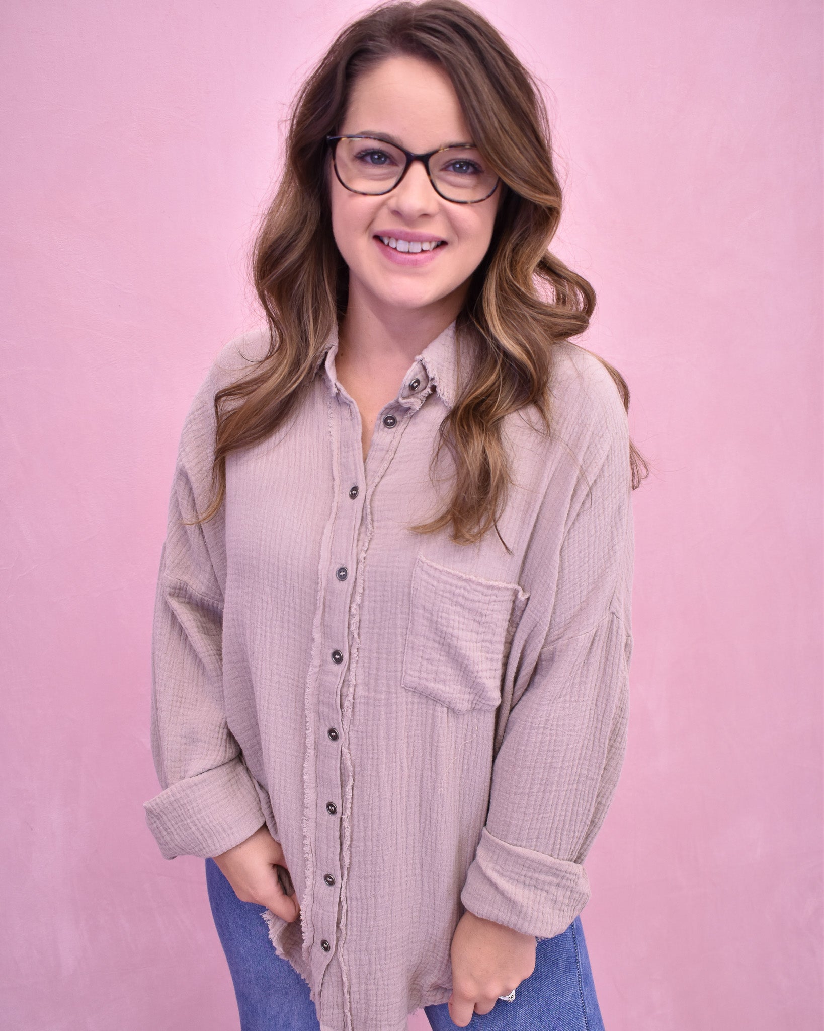 Woman wearing a light brown button-up shirt and blue jeans against a pink background