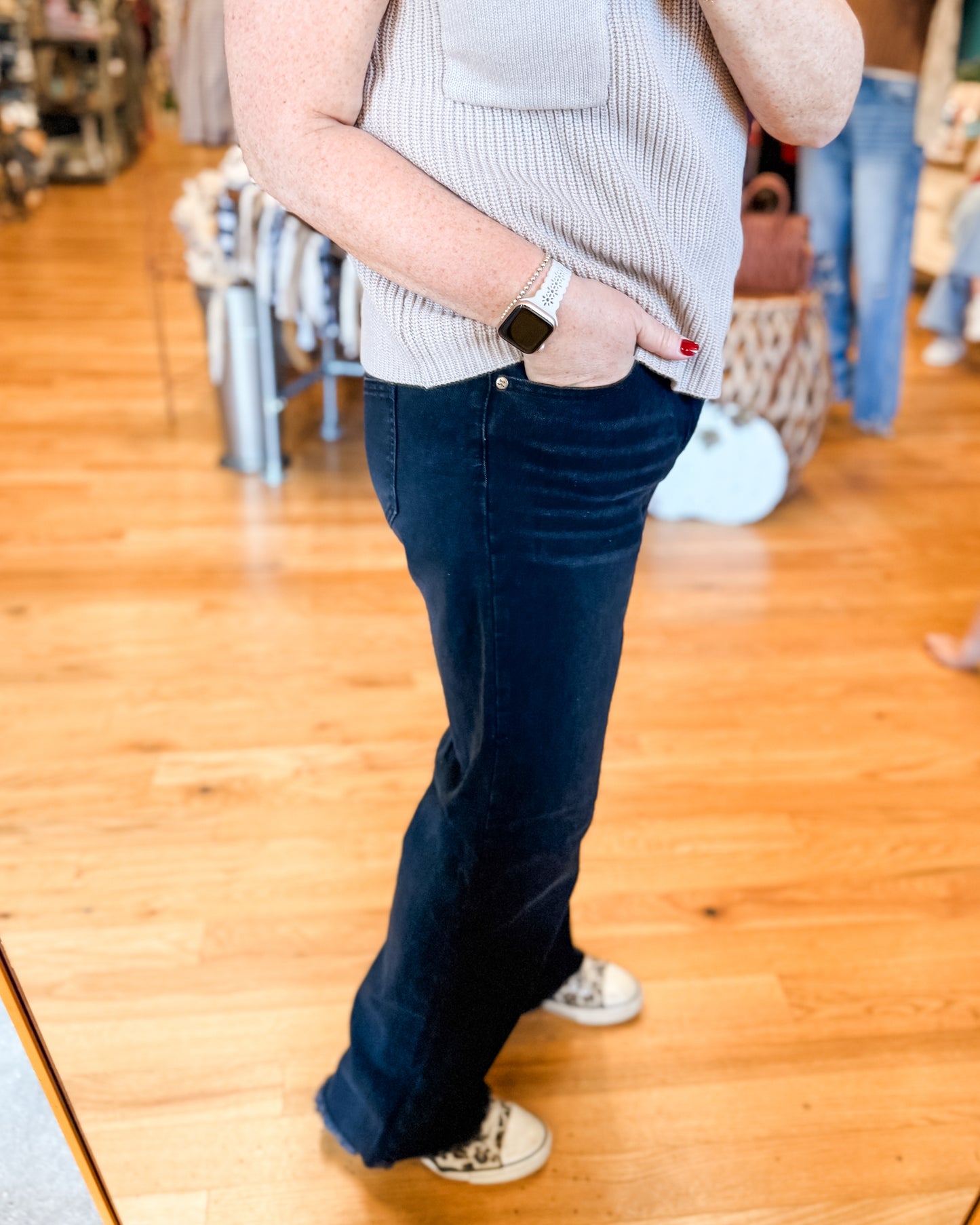 Person wearing a light gray sweater and dark blue jeans on a wooden floor.