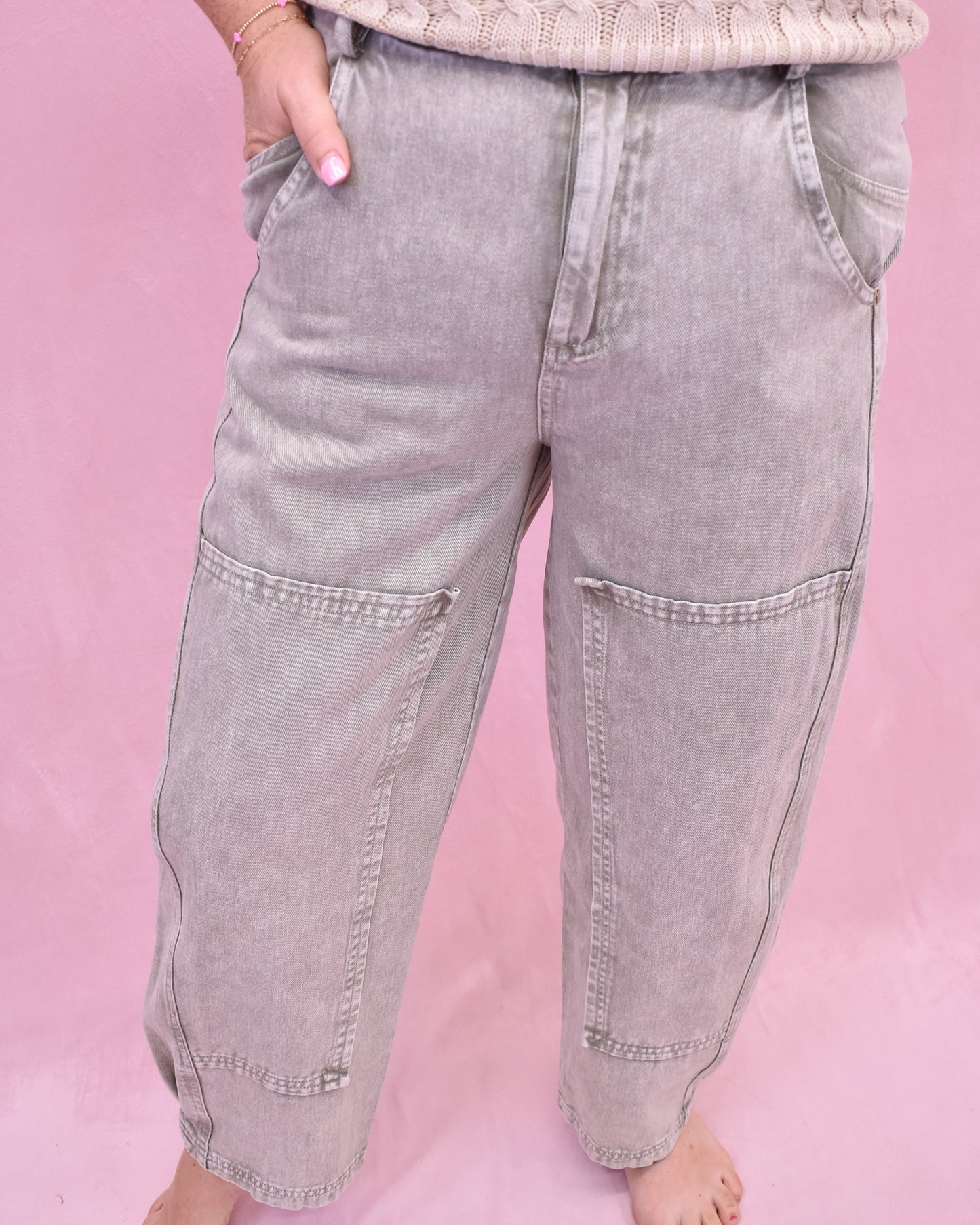 Person wearing light gray baggy jeans on a pink background