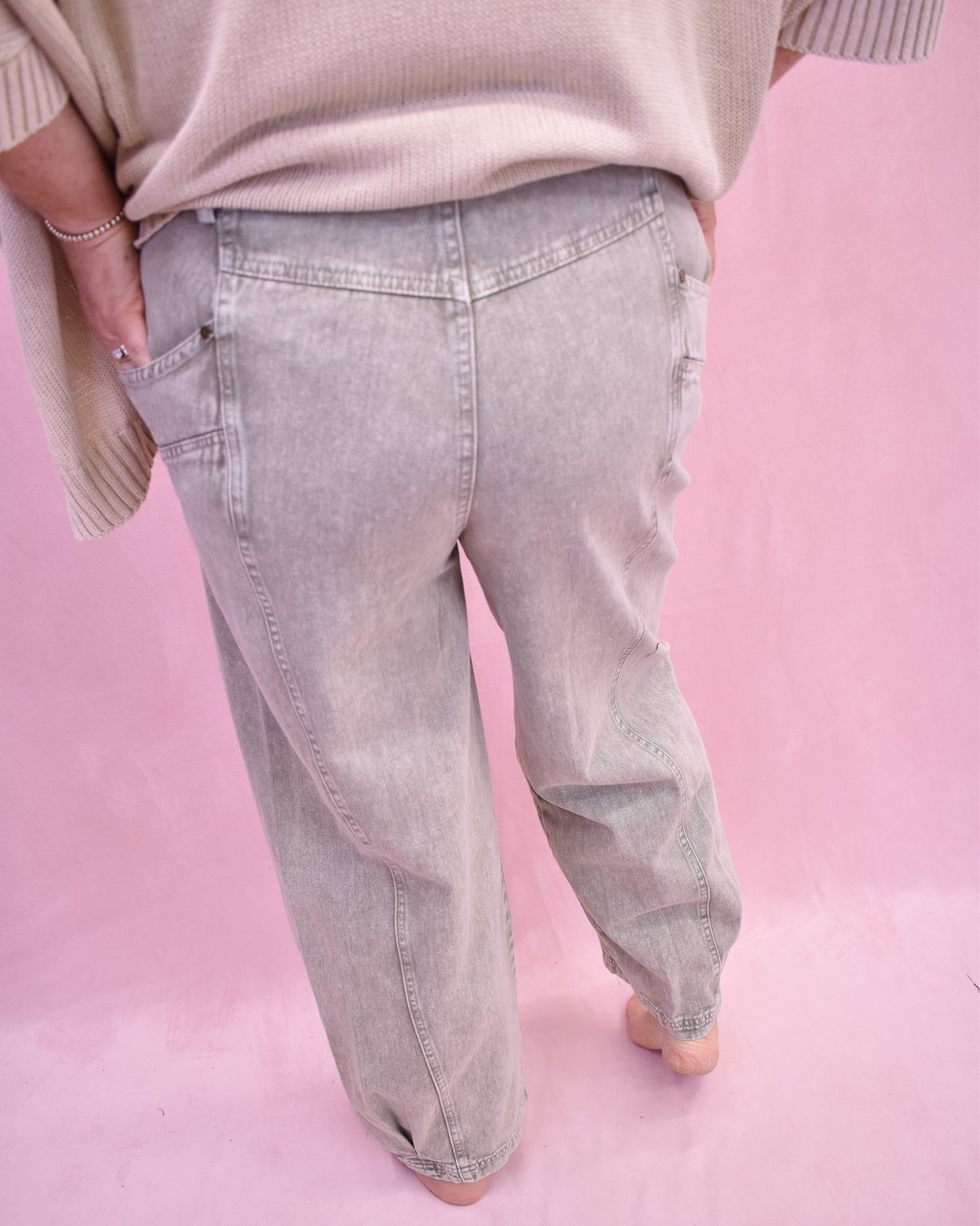 Person wearing light gray jeans and a beige sweater on a pink background