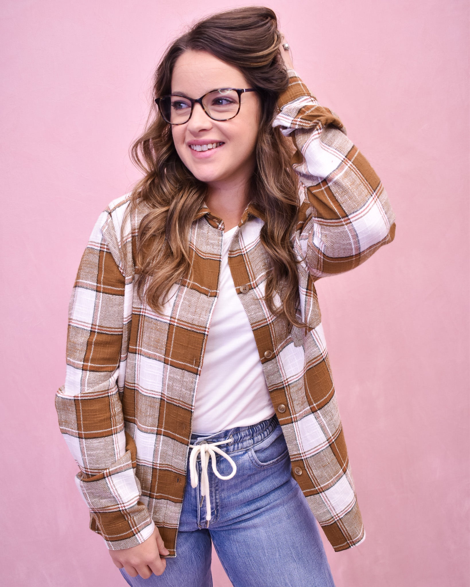 Woman wearing a plaid shirt and jeans against a pink background