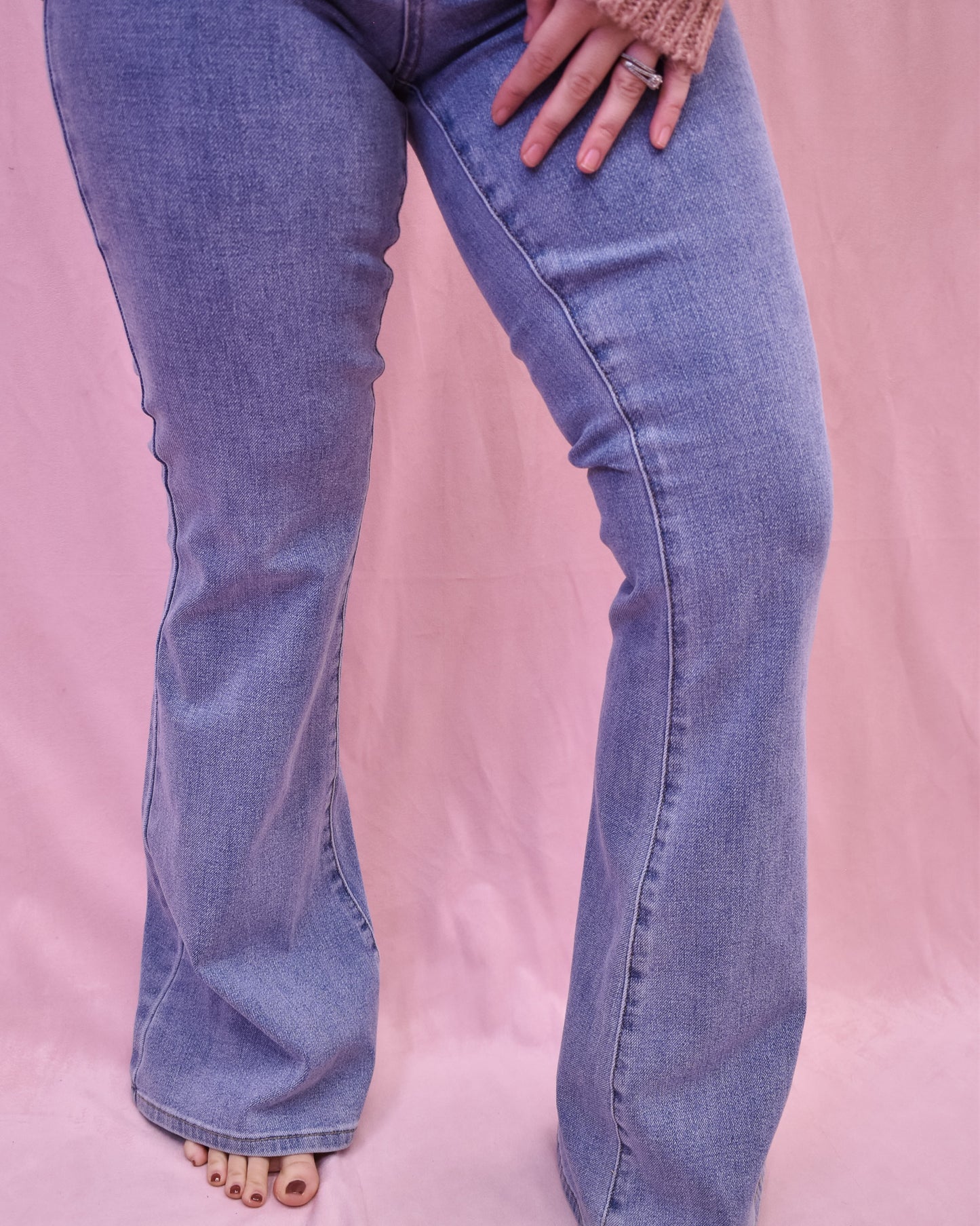 Flared jeans worn by a person on a pink background