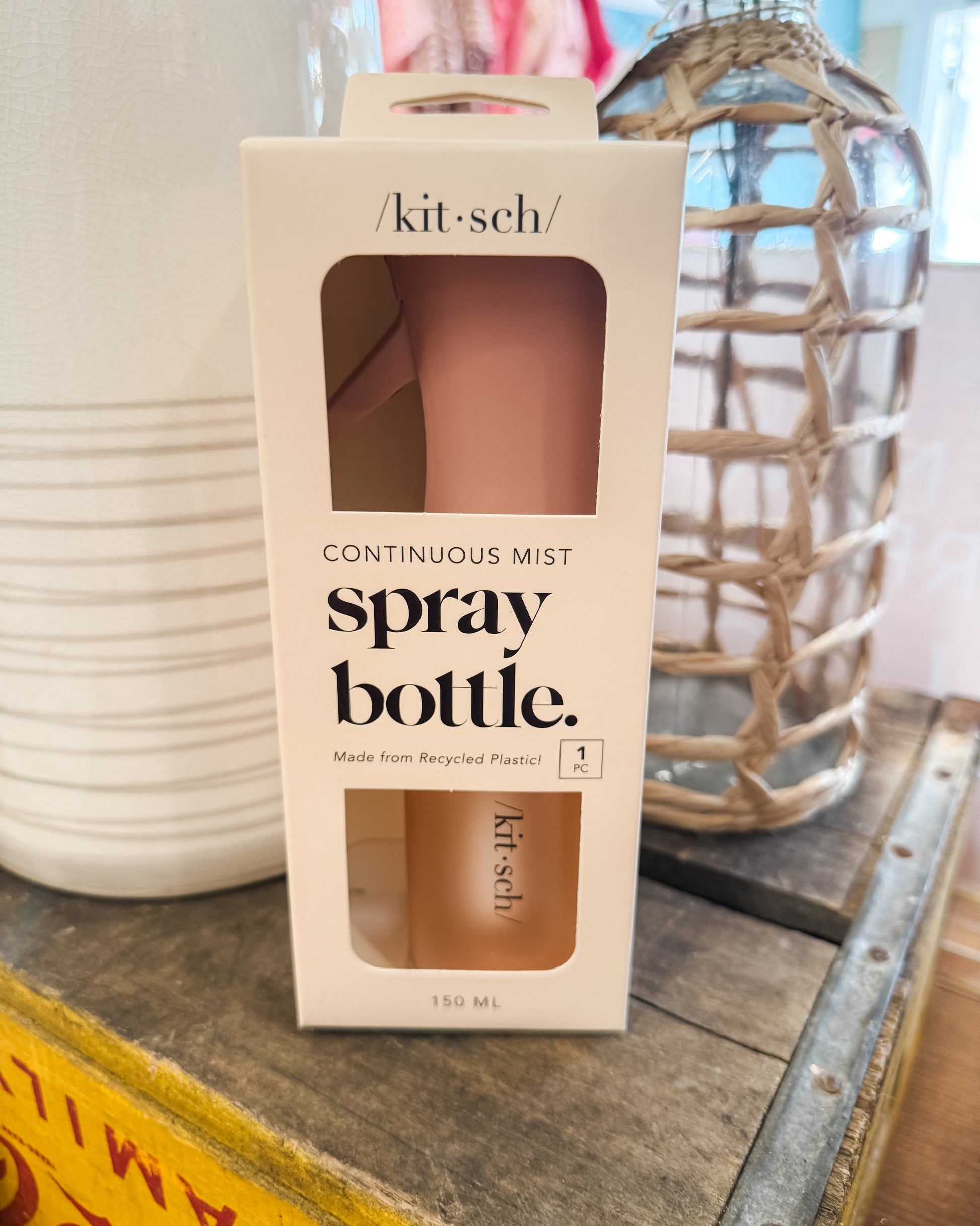 Kit-sch spray bottle packaging on a wooden surface with decorative items in the background