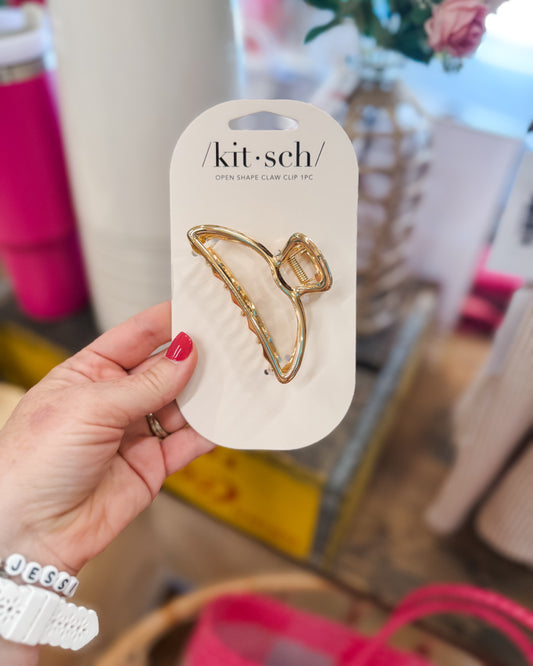 Gold hair clip on a 'kit-sch' branded card held by a hand with red nail polish.