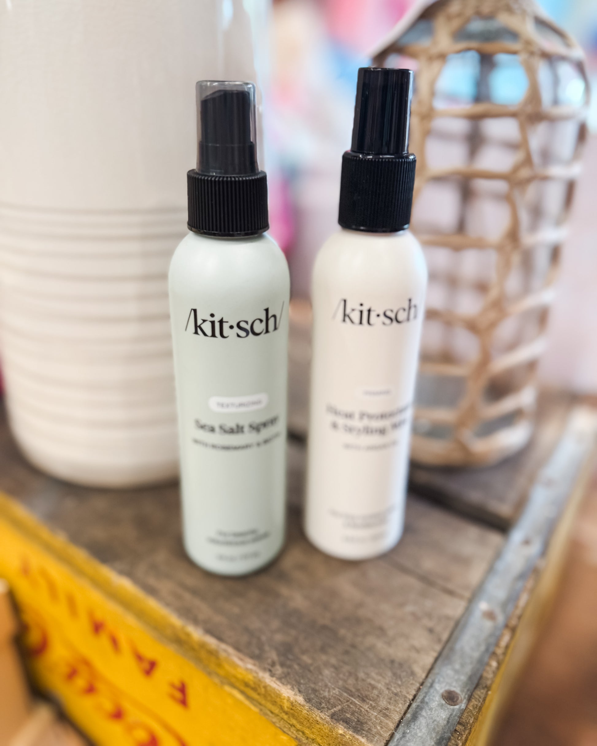 Two white spray bottles with black nozzles on a wooden surface, featuring the 'kitsch' brand.
