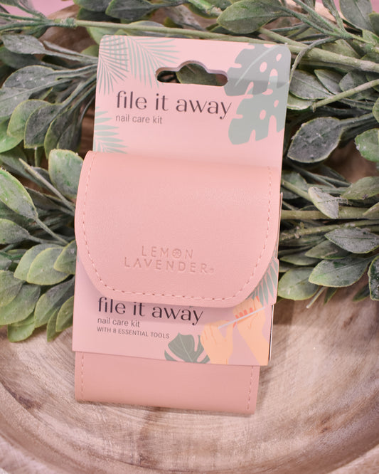 Pink nail care kit labeled 'file it away' on a wooden surface with green leaves in the background