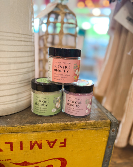 Three jars of 'let's get steamy' products on a wooden surface with a blurred background.