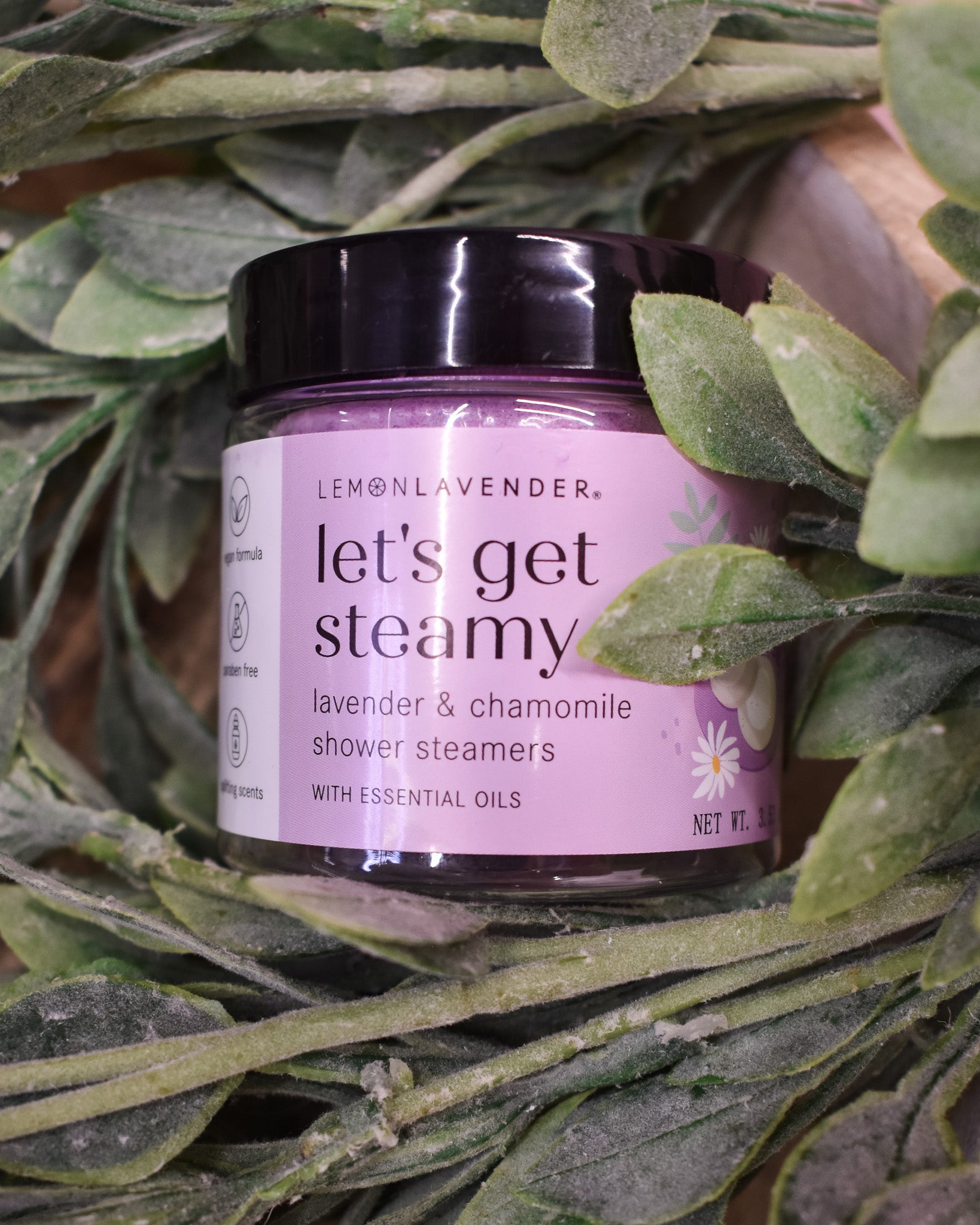 Jar of 'let's get steamy' shower steamers surrounded by green leaves