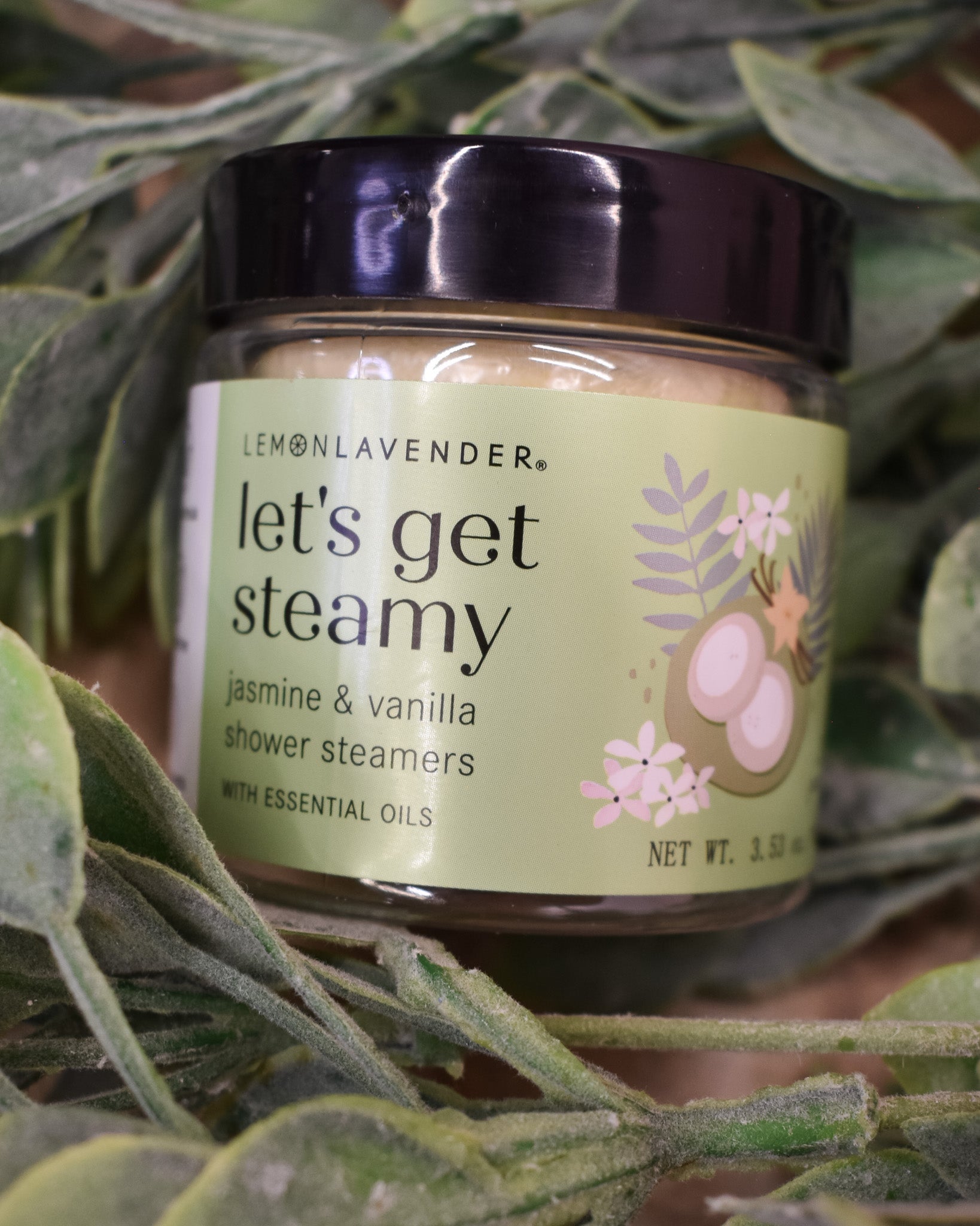 Jar of Lemon Lavender 'let's get steamy' jasmine & vanilla shower steamers surrounded by green leaves.