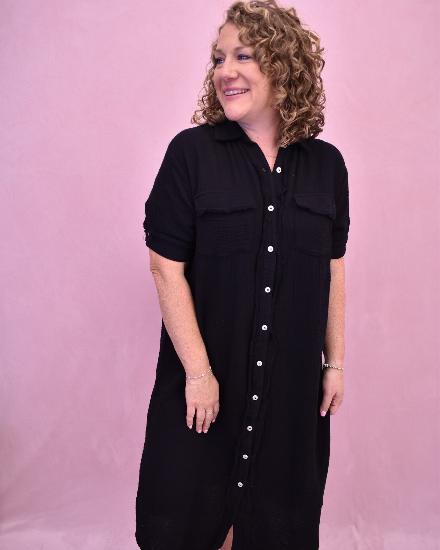 Woman wearing a black dress with white buttons against a pink background