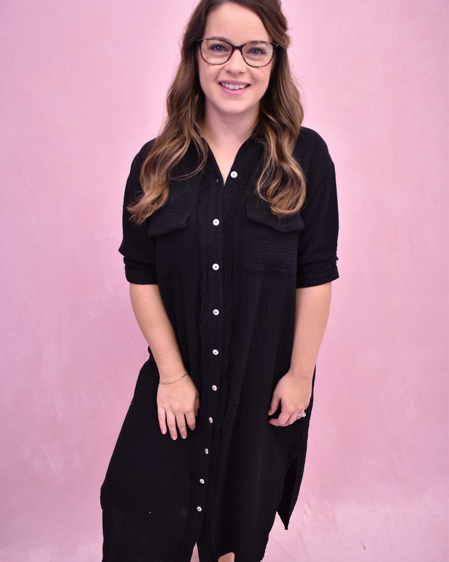 Woman wearing a black dress with white buttons against a pink background