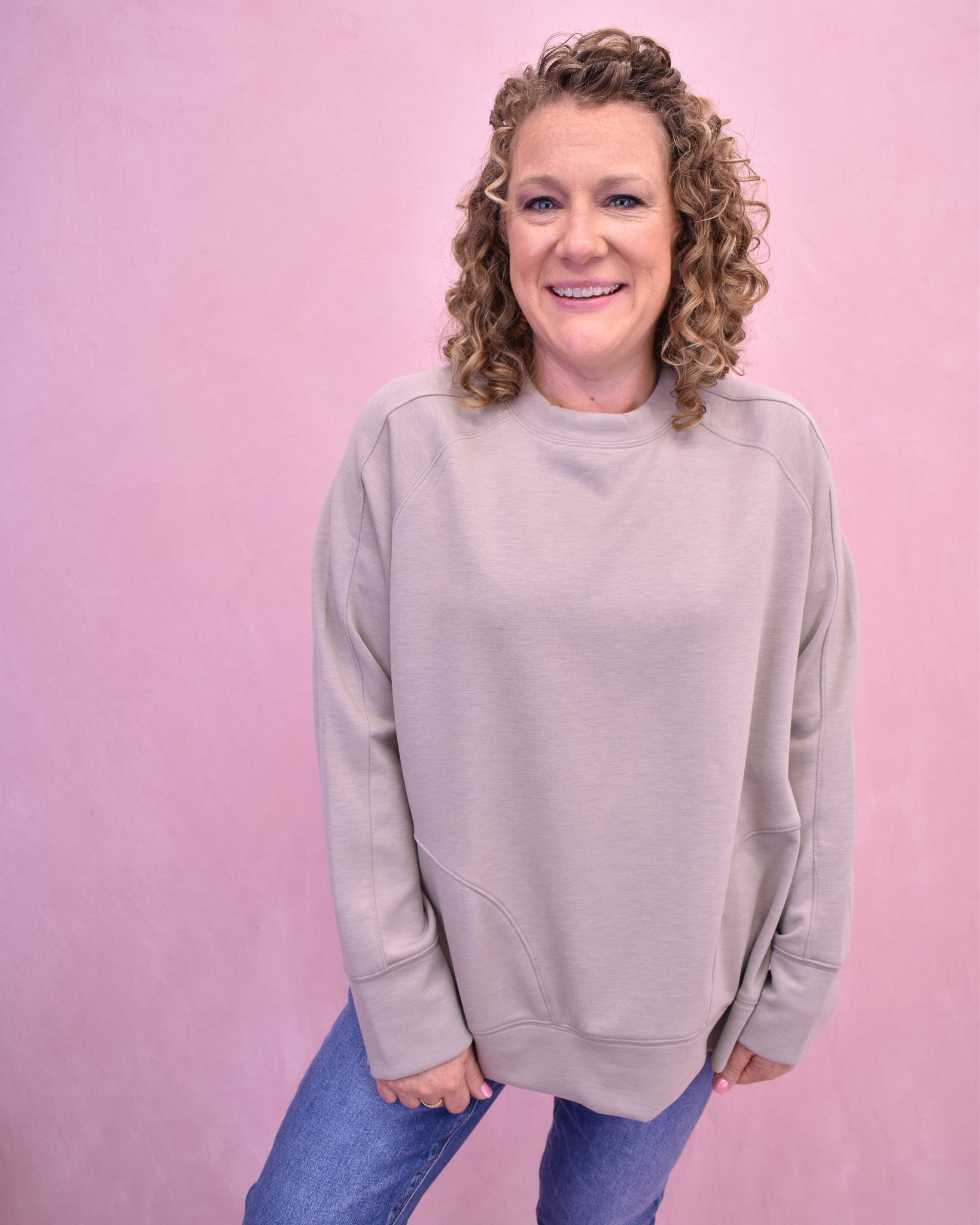 Person wearing a light gray sweatshirt against a pink background