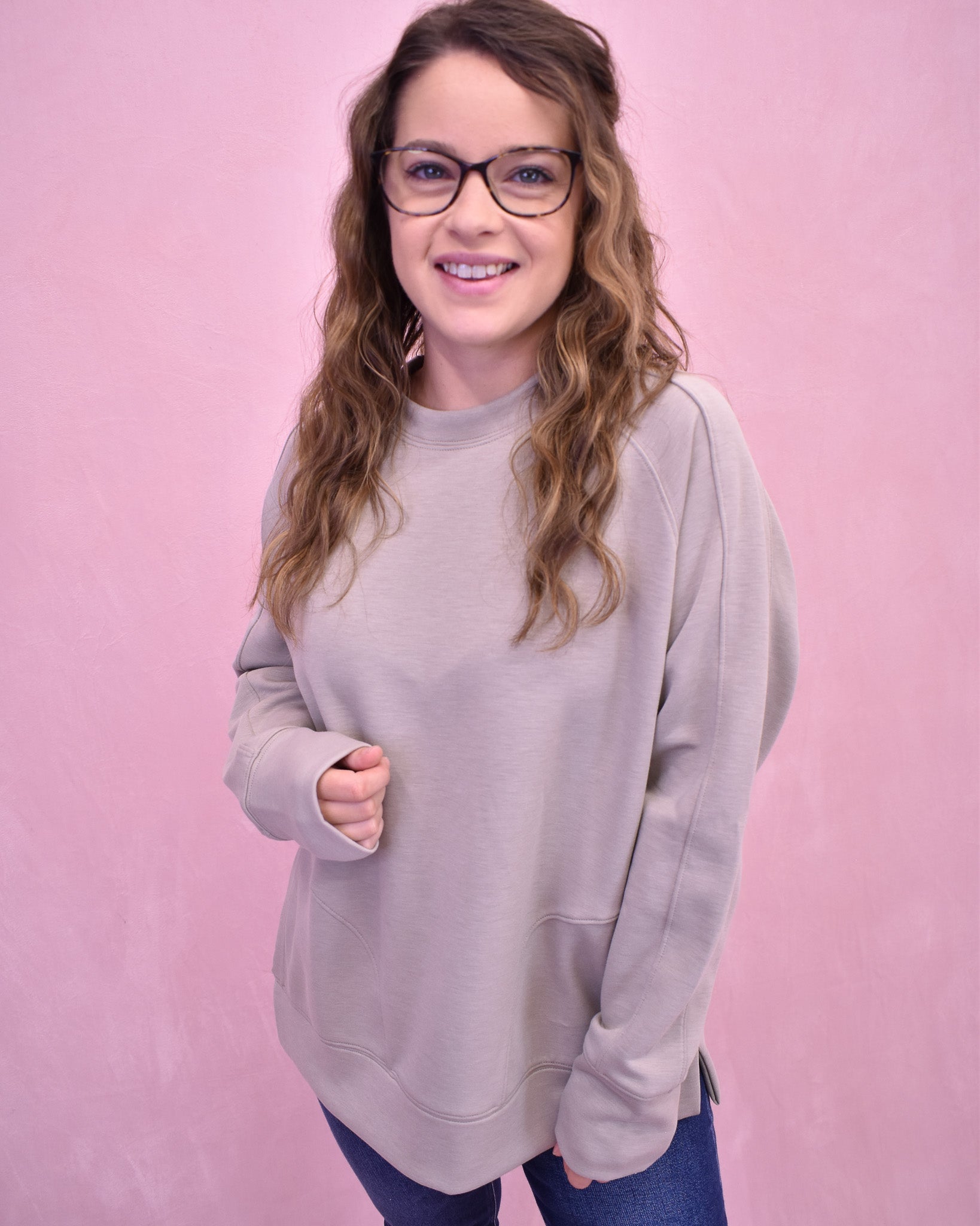 Woman wearing a light gray sweatshirt against a pink background