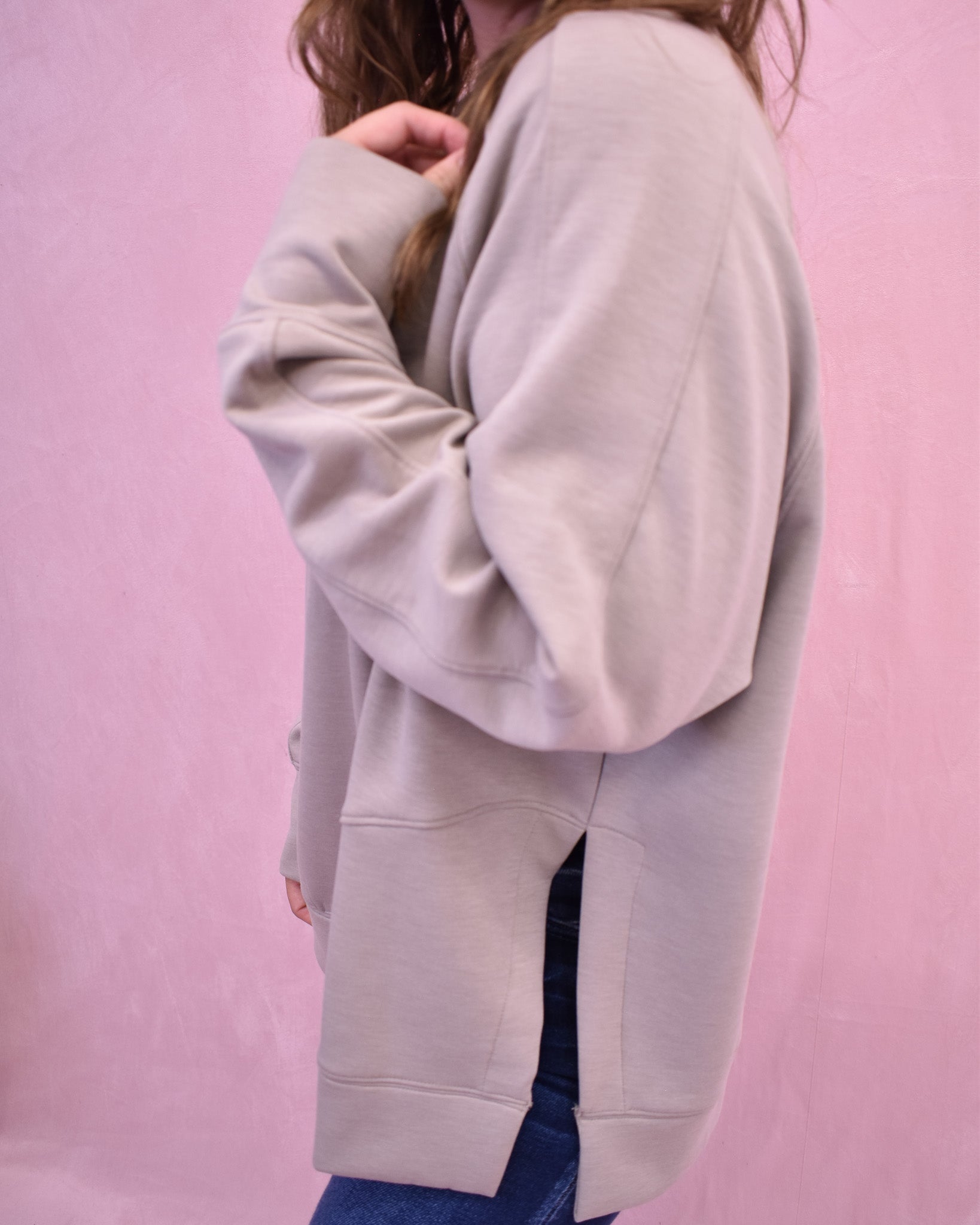 Person wearing a light gray hoodie against a pink background
