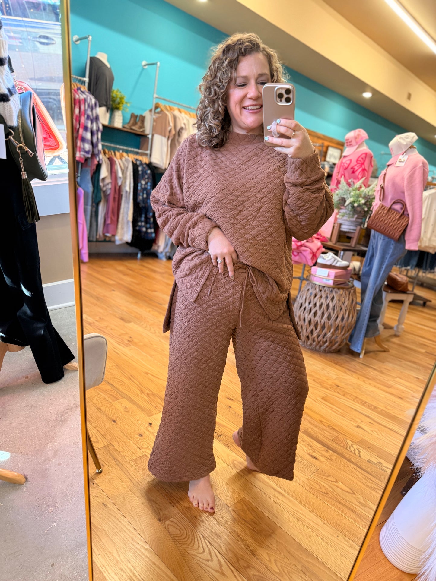 Woman taking a mirror selfie wearing a brown textured outfit in a store.