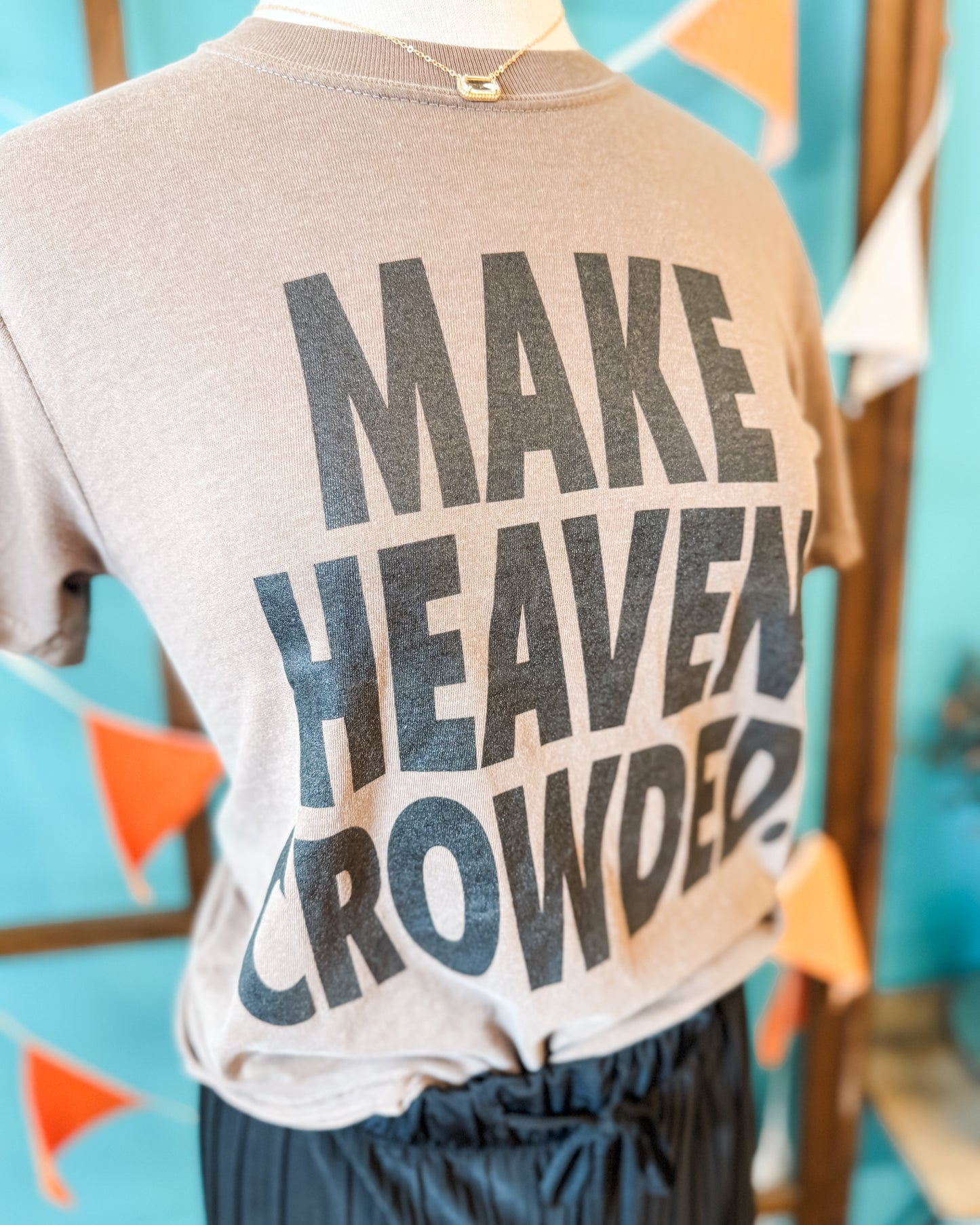 T-shirt with 'MAKE HEAVEN CROWDED' text on a mannequin against a colorful background
