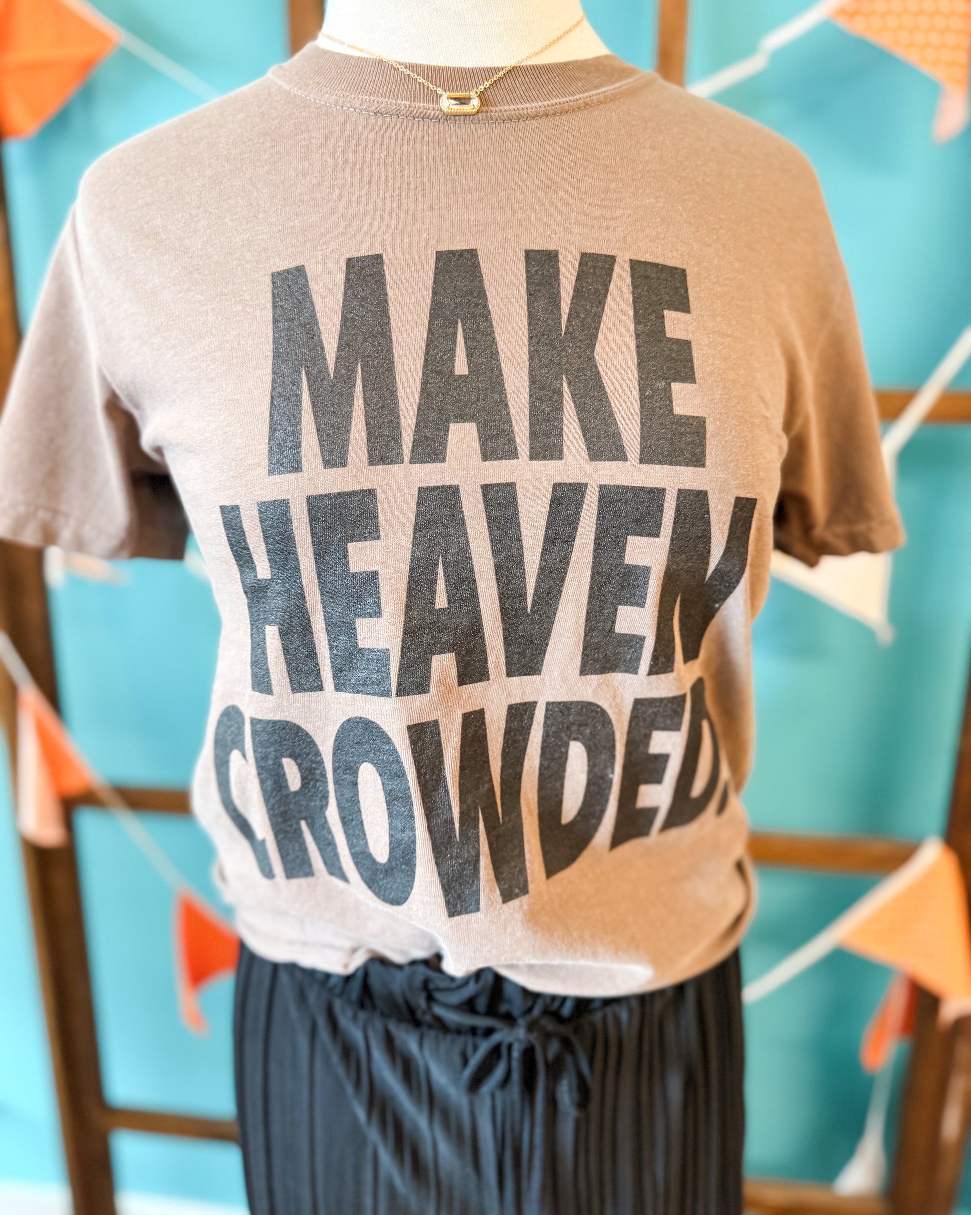 T-shirt with 'MAKE HEAVEN CROWDED' text on a mannequin against a colorful background